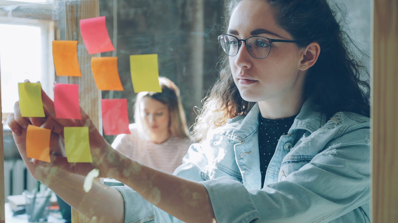 Woman analyzes sticky notes on glass. — photo by Vitaly Gariev on Unsplash