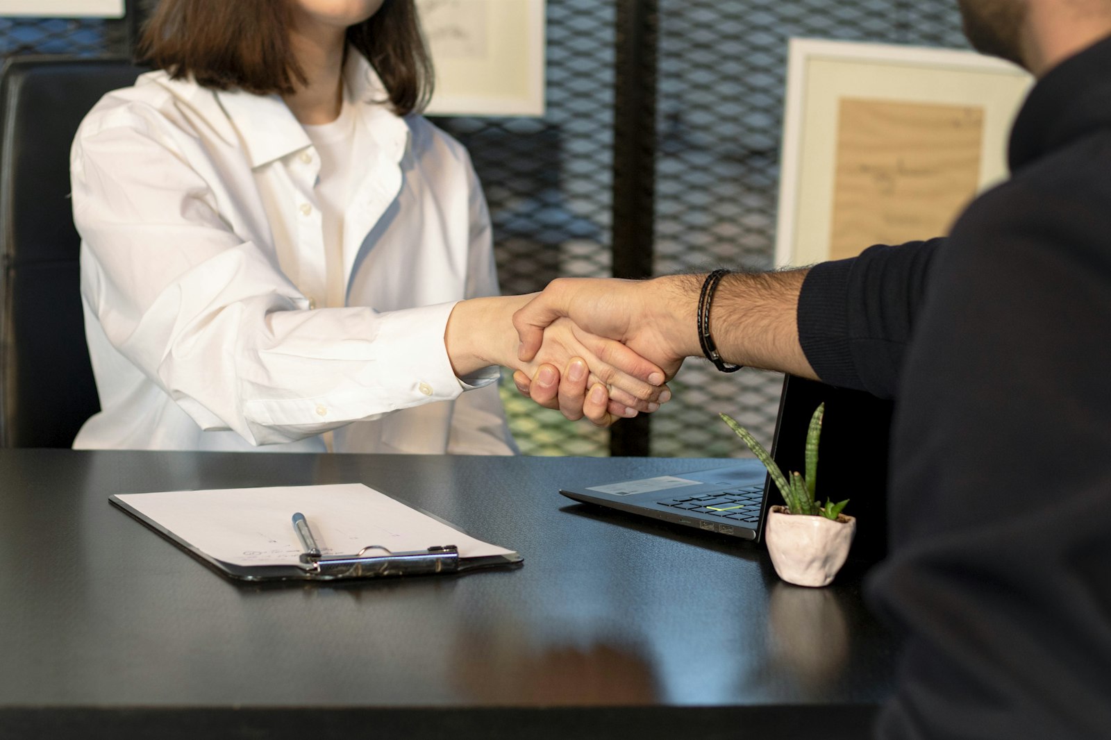 A man and a woman shaking hands in front of a laptop — photo by Mina Rad on Unsplash