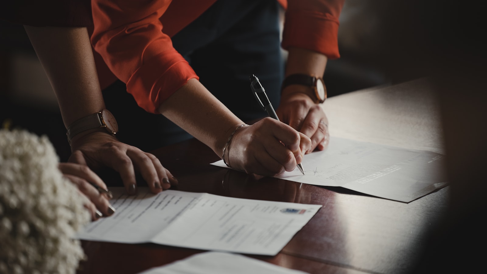 Person in orange long sleeve shirt writing on white paper — photo by Romain Dancre on Unsplash